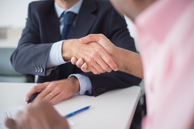 Person wearing a suit and tie shaking hands with another person in a pink shirt